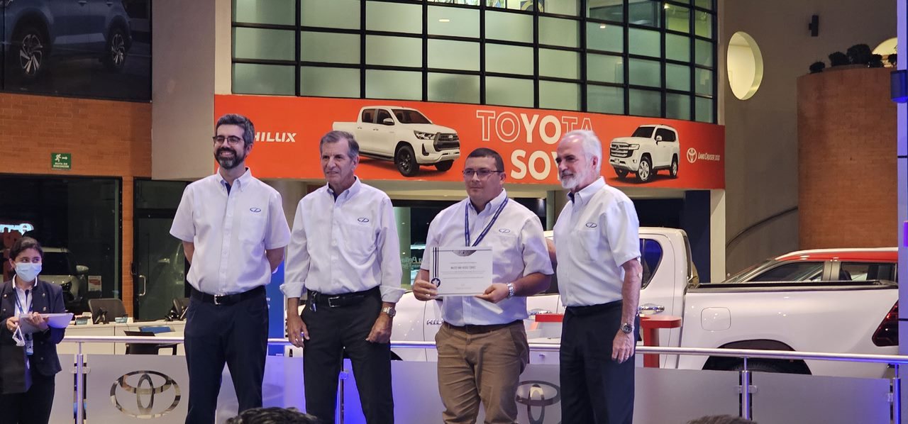Walter Araica recibiendo un reconocimiento de ventas en un evento
                      de la marca, junto a tres directivos.